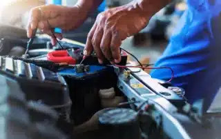 Mechanic diagnosing a car’s electrical system with a multimeter at an auto repair shop.