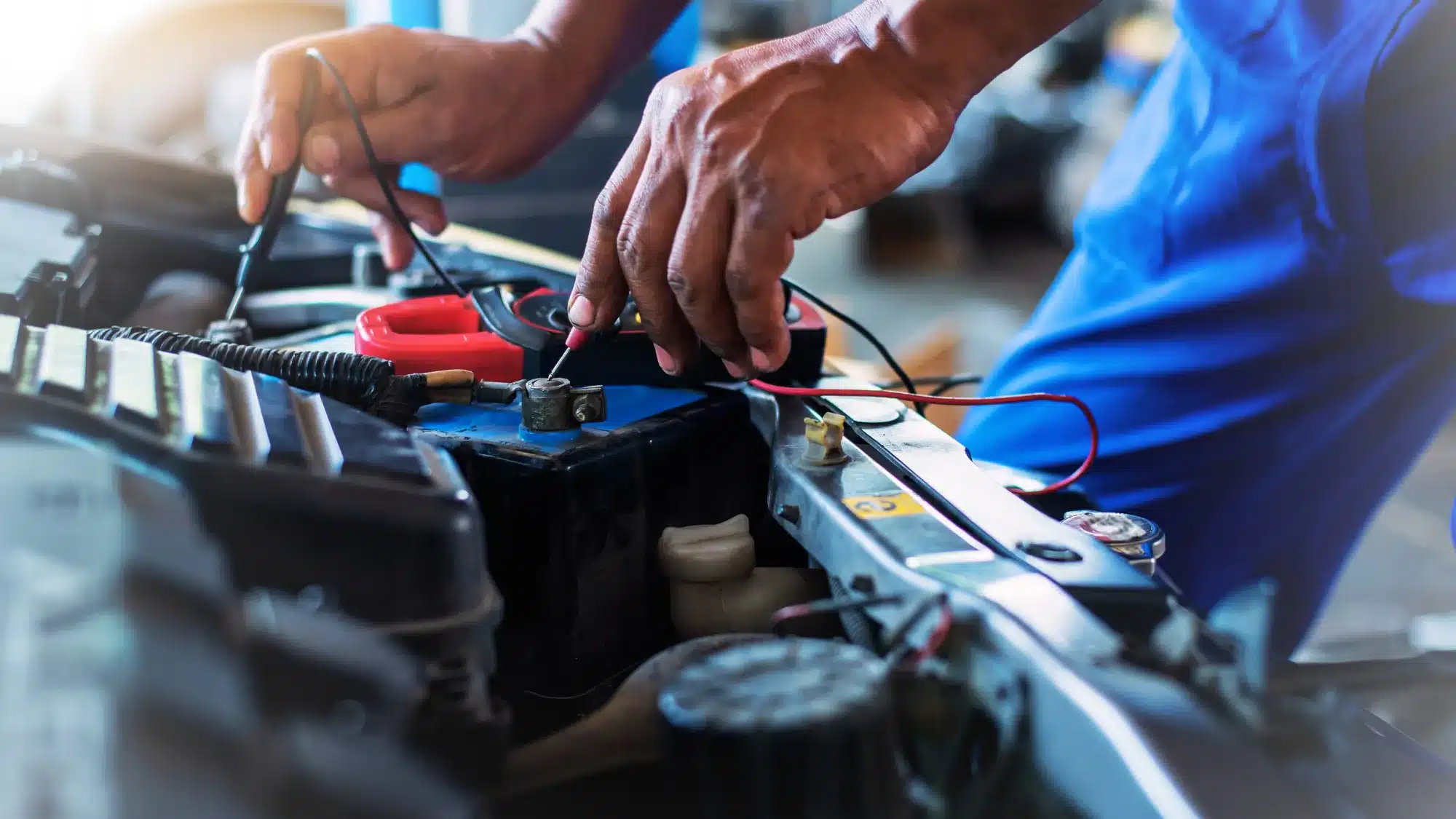 Mechanic diagnosing a car’s electrical system with a multimeter at an auto repair shop.