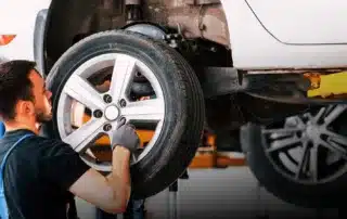 Mechanic servicing a vehicle's brakes and checking AC and electrical systems in a professional garage.