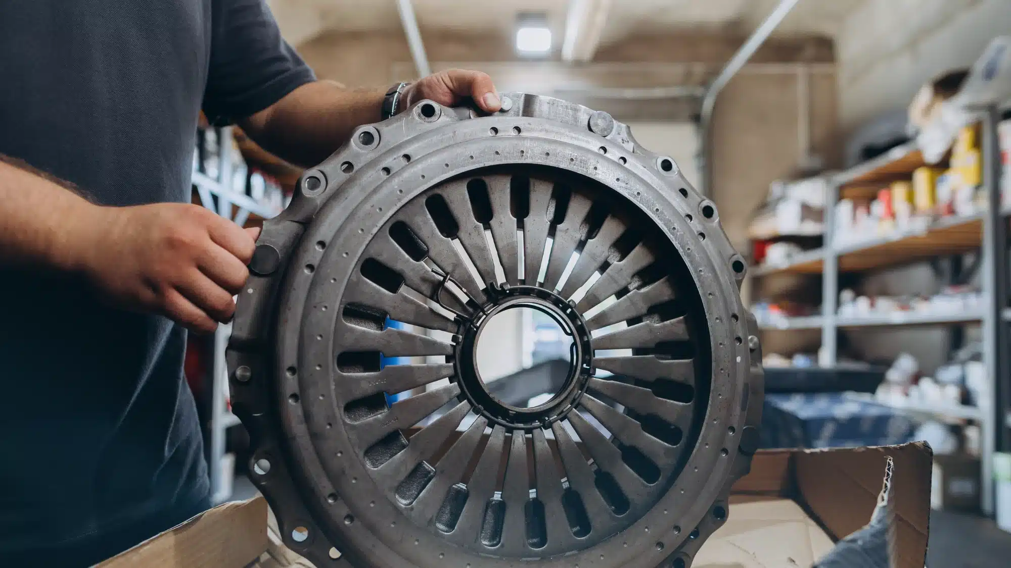Close-up view of a mechanic's hands inspecting a worn clutch plate in an automobile workshop.